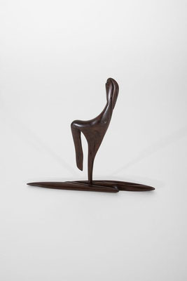 Abstract minimalist wood sculpture featuring a stylized, slender figure balanced on a horizontal needle-shaped base, crafted from dark brown polished hardwood with delicate organic grain details, isolated on a white studio background.