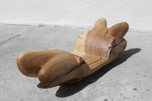 undulating oak wood sculpture V1558 by Jörg Pietschmann, showcasing its smooth grain and dynamic organic curves, shot on concrete against a white wall.