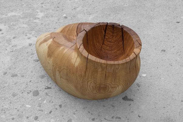 organic ash wood sculpture V1568 by Jörg Pietschmann. The smoothly carved piece evokes the intimate, protective curves of a woman's lap, featuring a prominent circular cavity at the top and flowing grain on a concrete floor.