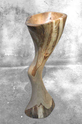 Organic oak wood bowl sculpture V1366 by Jörg Pietschmann, featuring a fluid, curved pedestal and a hollowed top, photographed outdoors against a weathered concrete wall.