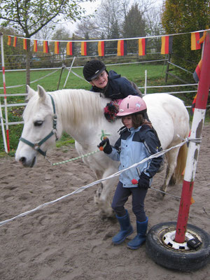 Das weiße Pony wird unter einer Girlande durchgeführt und der Junge auf dem Pferd muss sich nach vorne lehnen um durchzukommen. 