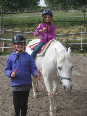 Das Mädchen macht auf dem Pferd eine spielerische Übung um die Hände ruhig zu halten. Sie balanciert einen Ball auf dem Löffel.