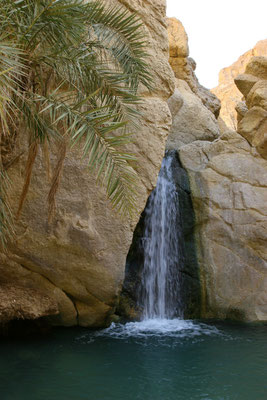 Vom zerstörten Dorf führt ein Weg in die Oase mit einem kleinen Wasserfall. Denn das Überleben dieser Oasen war nur durch ein unterirdisches Wasserleitungssytem möglich, das die Vorräte im Berg anzapft und über Kanäle weiterleitet.