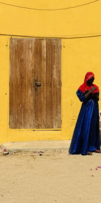 Die bunte Kleidung der afrikanischen Frauen im Kontrast zu den ockerfarbenen Häusern.