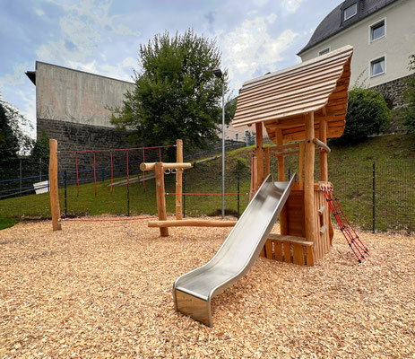 Kombinierter Kletter- und Hangelparcours mit Rutschenturm mit Satteldach aus Robinie mit Spieltresen und Boulderwand und einem Kletternetz.