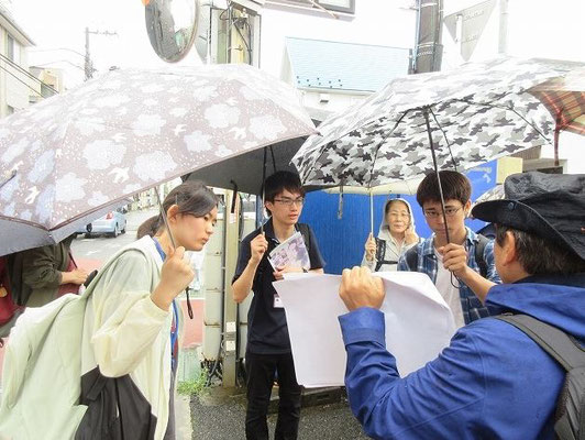 ・鎌倉郡衙跡で説明を聴く３人の高校生。 あいにくの雨でしたが熱心に耳を傾ける姿が印象的でした。鎌倉郡衙跡は鎌倉駅北口より高い位置にあり水の被害を免れています。 ・鎌倉郡衙跡  現在の市役所、御成小学校の一帯の遺跡です。(今小路西遺跡) 律令時代の相模国は8つの「郡」に分かれていてこの地には「鎌倉郡」がありました。昭和54年、今小路西遺跡で天平五年銘の木簡が発見されました。(奈良時代732年、長さ約20㎝)