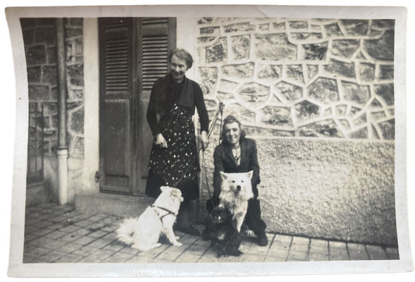 Zwei ältere Frauen mit ihren beiden weißen Spitzen vor einem Haus