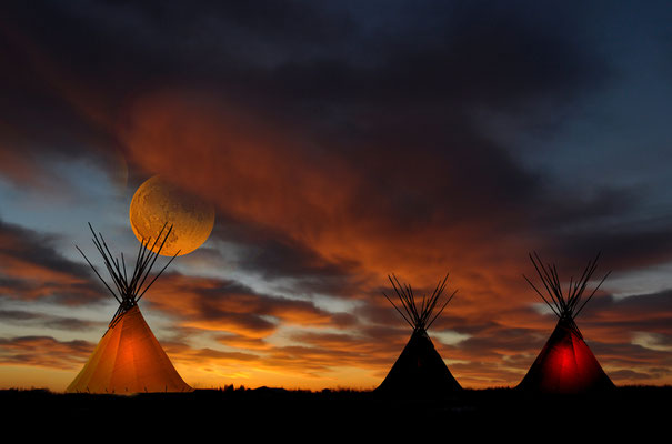 Night over the prairie. A romantic scene with three tipis and a low-hanging moon.