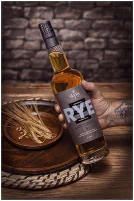 Rye Whisky Flasche in einer Hand mit Tattoos