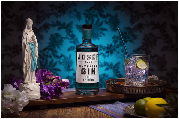 Josef Gin Flasche und Marien Figur auf Holzplatte und blauem Hintergrund