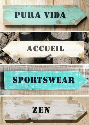Assemblage de flèches artisanales en bois peint en vert et blanc, avec des messages personnalisés comme "accueil", "zen", "sportwear" et "pura vida"