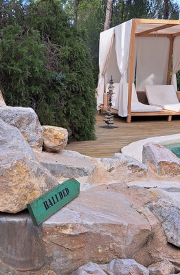 Flèche directionnelle décorative en bois peint en vert, posée en extérieur sur des rochers, avec un lit à baldaquin en fond