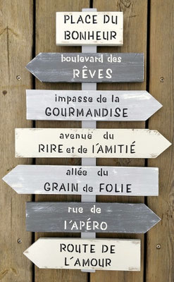 Panneau fléché dans des tons gris, texte peint en noir et blanc avec des messages inspirants sur l'amour, l'amitié et le bonheur