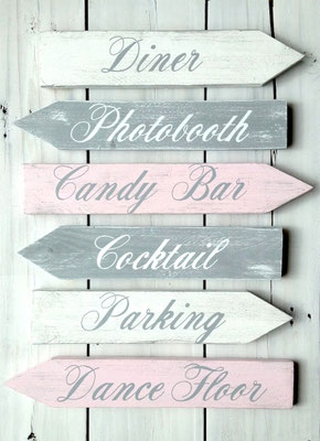 Flèches de mariage bois gris, blanc et rose, texte "Diner", "Cocktail", "Parking" ou "Dancefloor" peints en blanc et gris, posées sur fond bois blanc