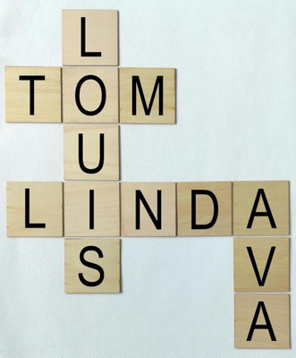 Scrabble en bois de balsa clair, personnalisé avec des prénoms en noir, sur un support mural blanc