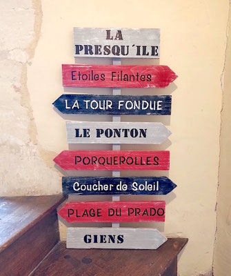 Panneau directionnel rouge, gris et noir posé sur un escalier bois personnalisé avec des lieux comme Porquerolles ou Giens