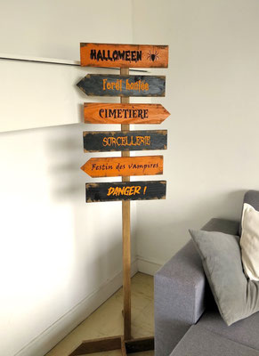 Panneau directionnel en bois décoratif pour Halloween, peint en noir et orange posé dans un salon à côté d'un canapé