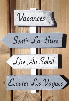 Panneau de direction gris et blanc en bois, avec une maxime calligraphiée en noir par flèche