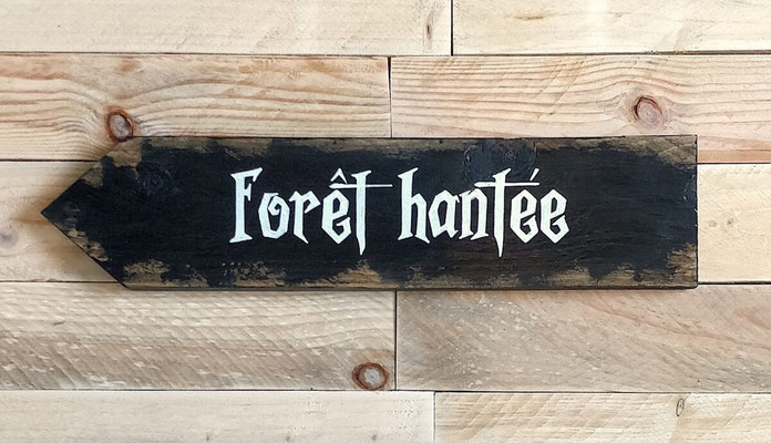 Flèche décorative d'Halloween peinte en noir, texte personnalisable blanc, posée sur un fond bois