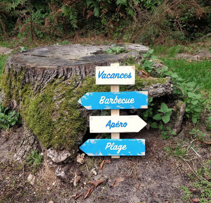 Panneau de direction fléché bleu outremer et blanc, susur le thème des vacances, posé en extérieur devant une souche d'arbre