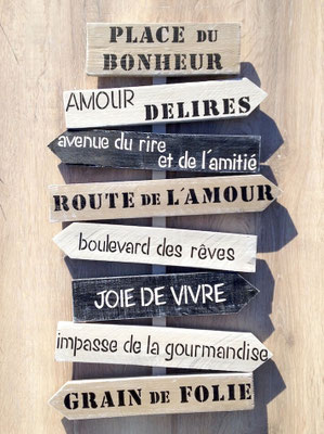 panneau directionnel noir et beige sur fond bois personnalisé avec des messages inspirants en noir et blanc sur le thème de la joie de vivre, du rire et de l'amitié