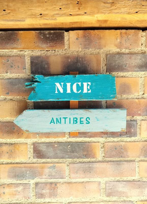 Panneau directionnel personnalisé dans un style bois flotté turquoise et blanc avec les villes de Nice et Antibes peintes à la main