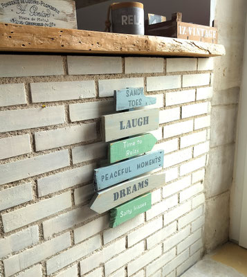 Panneau directionnel peint en mastic, vert et bleu clair, inscriptions personnalisées peintes à la main accroché à un mur en brique blanc