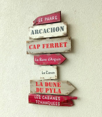 Panneau de direction personnalisé bois, peinture rouge et beige, villes peintes en couleur Cap Ferret , Arcachon, Dune du Pyla, accroché sur un mur extérieur crème