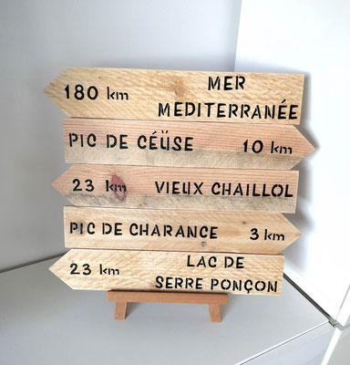 Flèches directionnelles en bois brut, villes personnalisées en noir, posées sur un chevalet en bois sur un meuble blanc