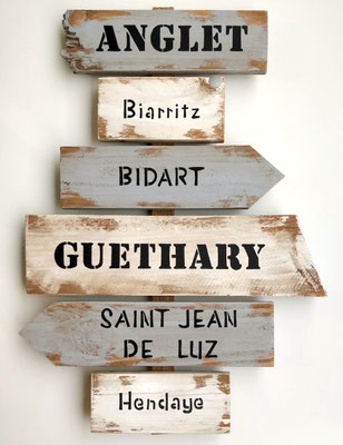Panneau de direction en bois vieilli avec plusieurs villes peintes en noir "St Jean de Luz", "Bidart" ou "Guethary"