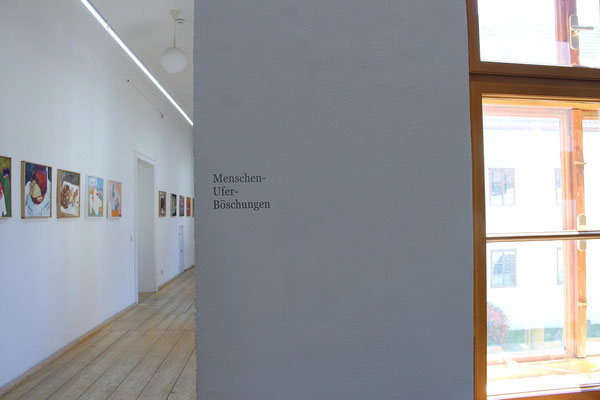 Ausstellung "Menschenufer" Foyer und Gang: "Süßes Brot", "Ich mal mir mal die Butter aufs Brot", "Horizont, Sessel, Schuh", "Türkis neben rosa und orange" und andere, Und Wandtext.