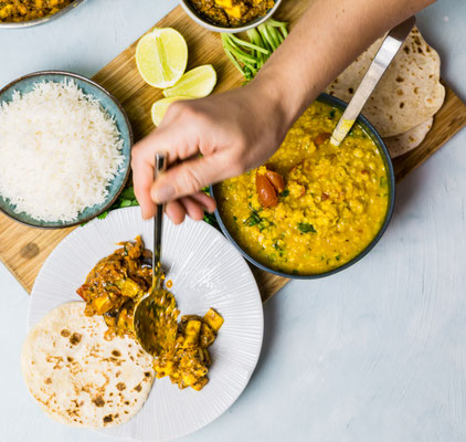 Indische Currys werden im Kochkurs von Bilou Kitchen in München gemeinsam angerichtet und serviert.