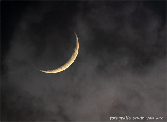Die Mondsichel zeigt sich zögerlich durch Wolkenlücken