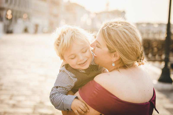 Mom holdings her child as they look out over a Venetian canal at sunset, capturing a tender and authentic family moment.