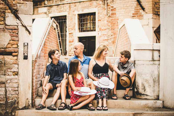 A family laughing genuinely together on a small, charming bridge in Venice, enjoying a candid moment during their family photoshoot.