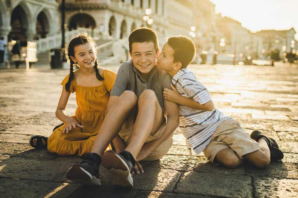 Venetian photographer interacting playfully with a child, eliciting a natural smile during a family photoshoot in a quiet campo, Venice.
