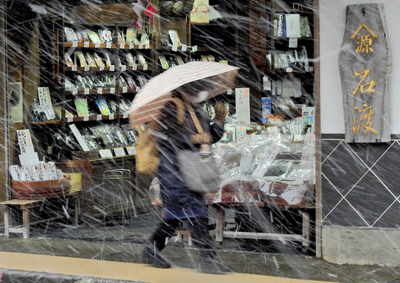 土産物店前を歩く女性に雪が容赦なく吹き付ける