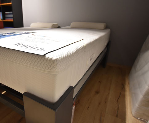Nahaufnahme einer weißen Matratze "femira" auf grauem Bettrahmen mit verstellbarem Lattenrost.