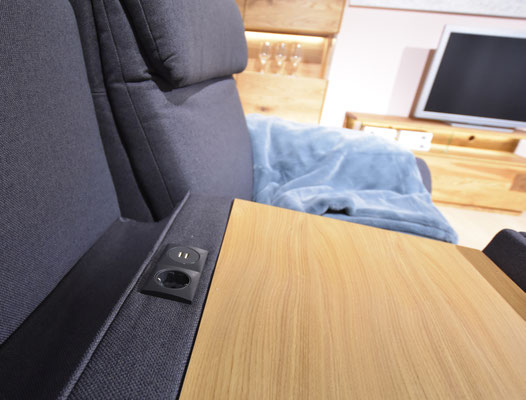 Ein dunkelgraues 2er-Sofa mit Holzplatte und integrierter Strom-Buchse in der Armlehne.