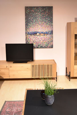 Farbenfrohes, abstraktes Gemälde über einem hellen Holz-TV-Schrank mit Fernseher.