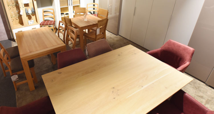 Essgruppe aus hellem Holz und roten Stühlen und weiteren Holztischen und passenden Stühlen.