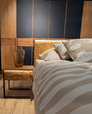 Modernes Schlafzimmer mit Holzbett, beleuchtetem Kopfteil und Nachttisch mit Glasvase.