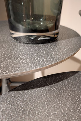 Nahaufnahme eines Glases auf einem kleineren, schwarz gehämmerten, runden Beistelltisch.