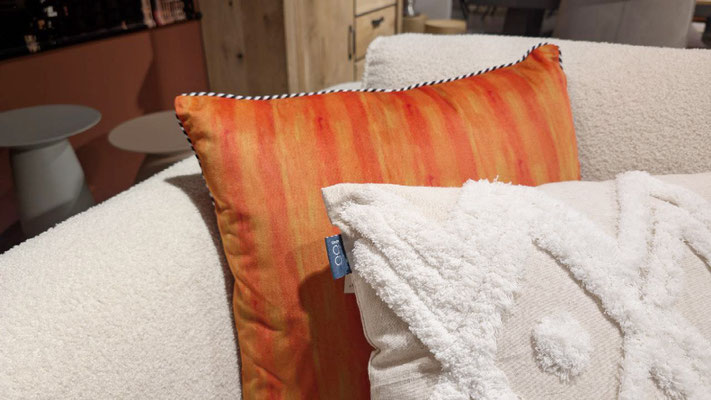 Oranges Kissen mit Streifenmuster auf einem cremefarbenen, flauschigen Sofa.