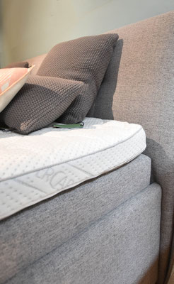 Boxspringbett mit grauem Stoffbezug, zwei Matratzen, Topper und Dekokissen im Set.