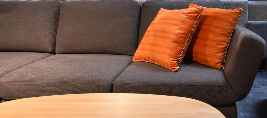 Dunkelgraues Sofa mit zwei gestreiften orangefarbenen Kissen und einem hellen Holztisch.