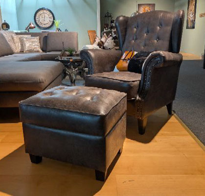 Brauner Leder-Ohrensessel mit Knopfheftung und passendem Hocker vor grauem Ecksofa.