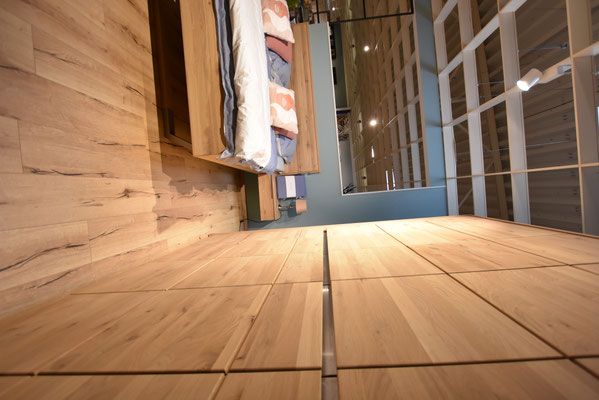 Schlafzimmer mit hellen Holzmöbeln, aus niedriger Perspektive aufgenommen und warm beleuchtet.
