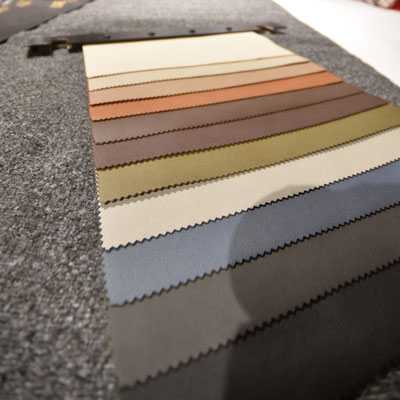 Fächer von Kunstleder- oder Stoffproben in Beige, Braun, Blau und Grau auf grauem Stoff.