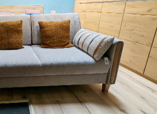 Hellgraues Schlafsofa mit braunen Kissen und einem gestreiften, beigen Zierkissen.